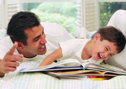 hisp dad preschool son reading on bed laughing