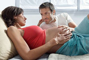 pregnant-couple-on-bed-touching-tummy