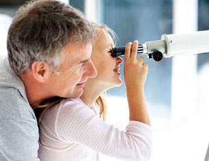 Cute young girl looking through telescope with her father