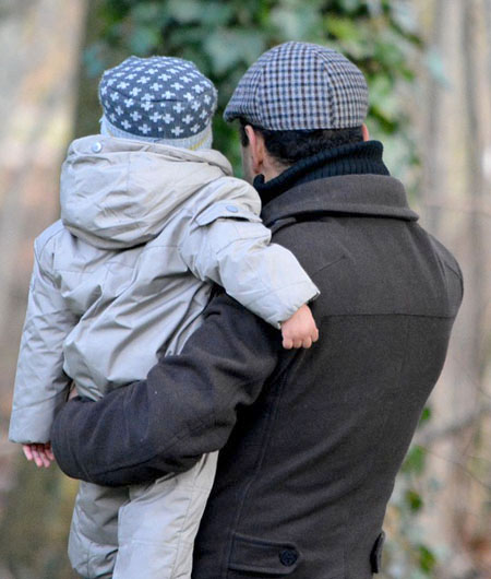 father holding toddler coats & hats looking away